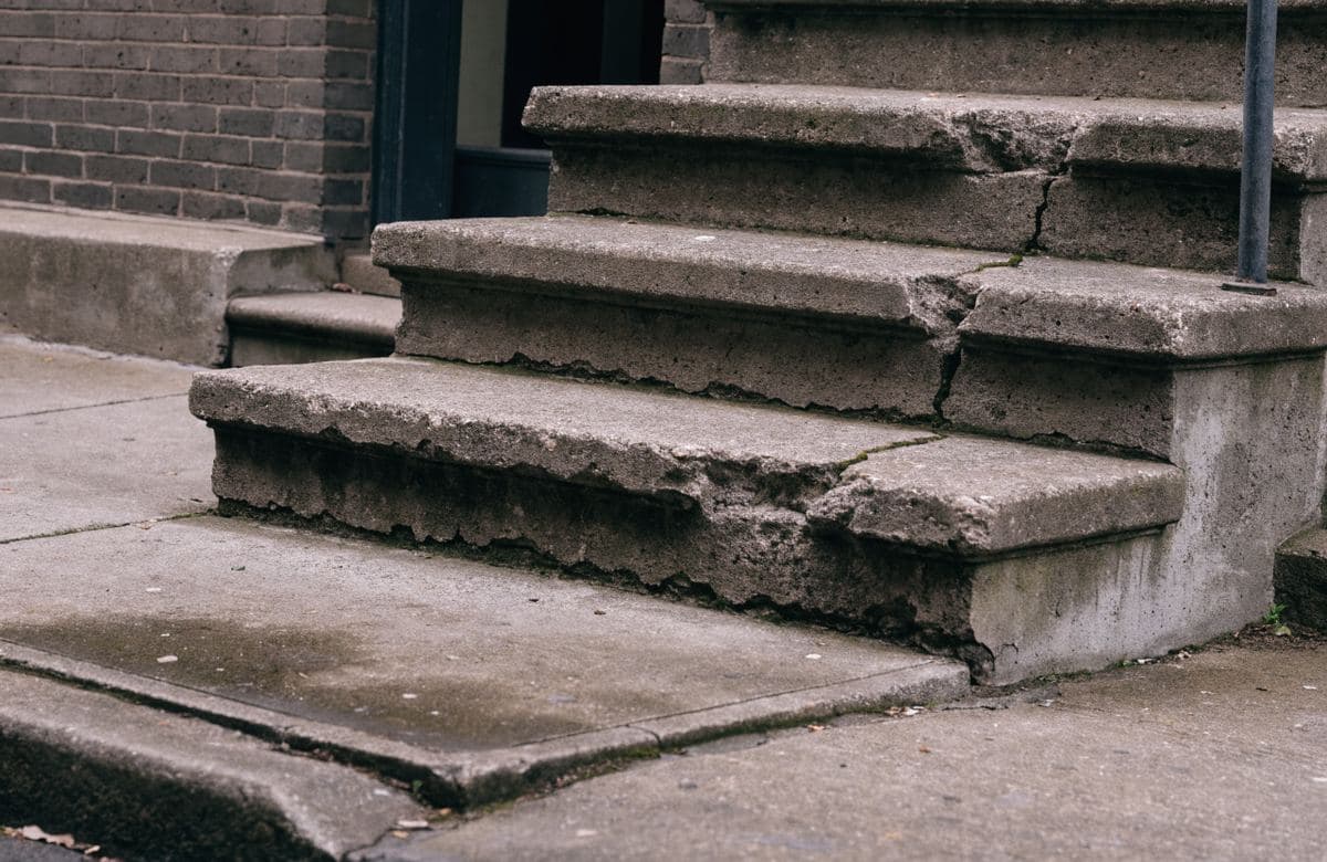 Illustrative example of concrete entry steps with a spalled edge, cracking and a settled sidewalk slab