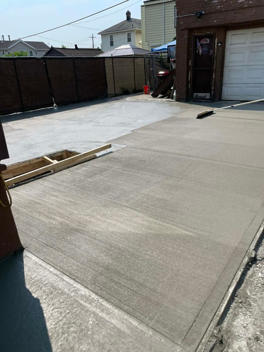 Finished concrete surface with visible control joints beside a residential property