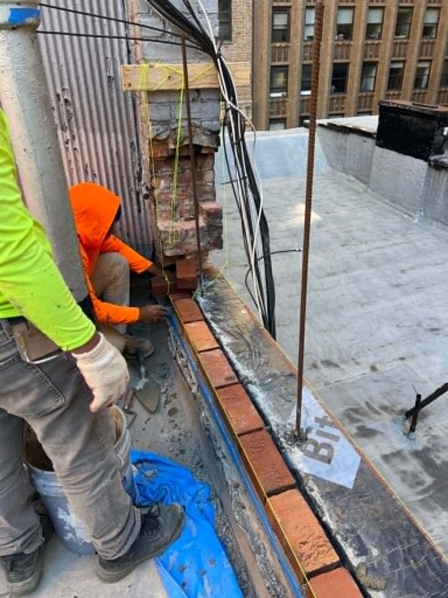 Mason repairing the mortar joints at the base of a brick wall