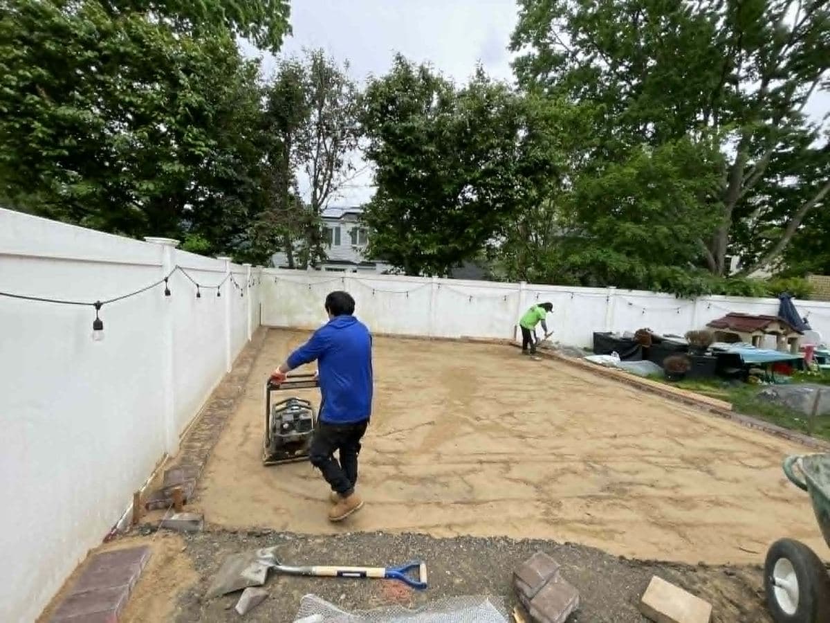 Worker running a plate compactor across a newly installed paver surface