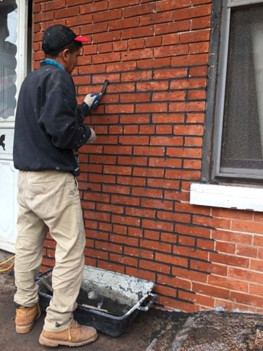 Worker treating the surface and joints of a red brick wall beside a window
