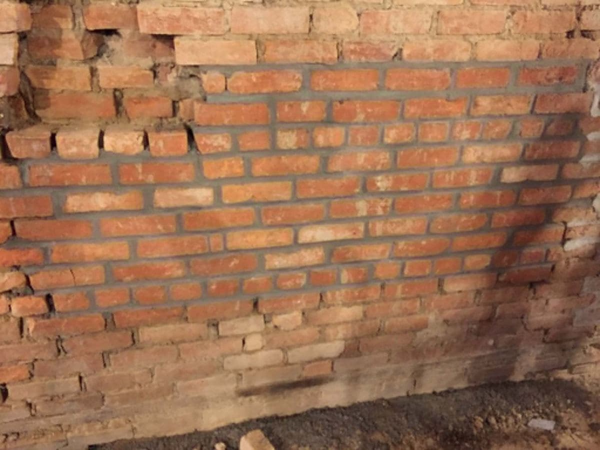 Brick wall with aged mortar joints under review before repointing