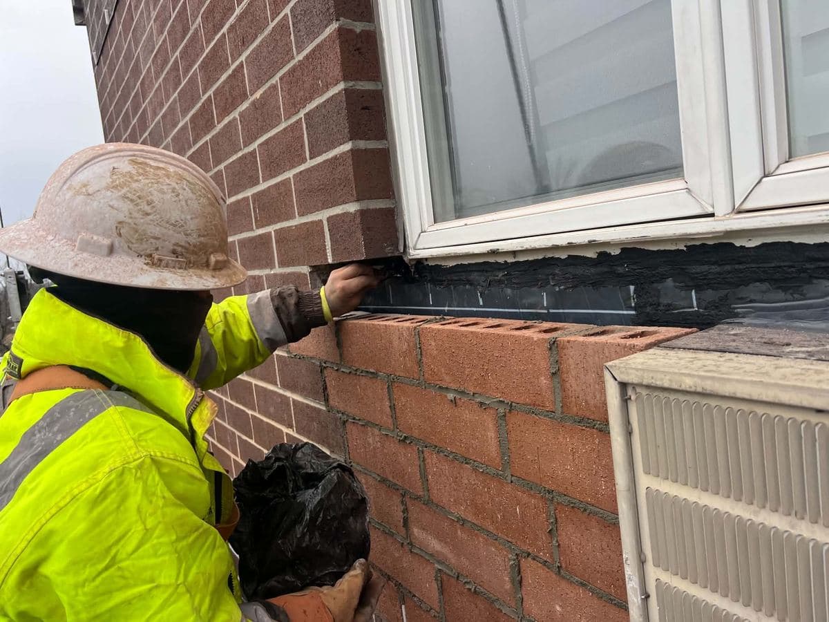 Worker sealing the masonry joint below a window with waterproofing material